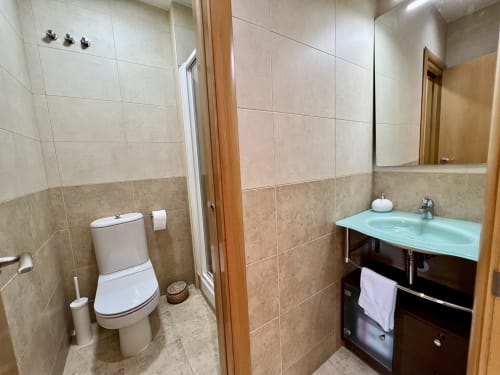 Baño moderno en Apartamentos J&A Terrassa con inodoro, lavabo turquesa, espejo y paredes alicatadas