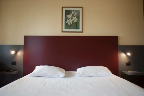 Chambre moderne de l'hôtel Mape à Dampierre-en-Burly avec tête de lit bordeaux, literie blanche et tableaux floraux