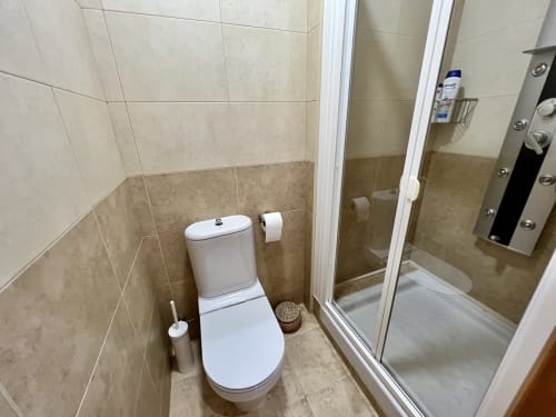 Baño moderno en J&A Apartments Terrassa con inodoro blanco, cabina de ducha de cristal y paredes de azulejos beige