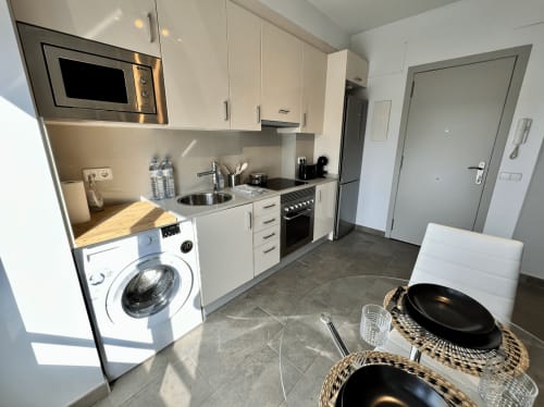 Cocina moderna en Apartamentos J&A Terrassa con muebles blancos, electrodomésticos de acero inoxidable, lavadora y zona de comedor