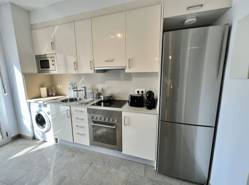 Cocina moderna en J&A Apartments, Terrassa con armarios blancos, electrodomésticos de acero inoxidable y lavadora