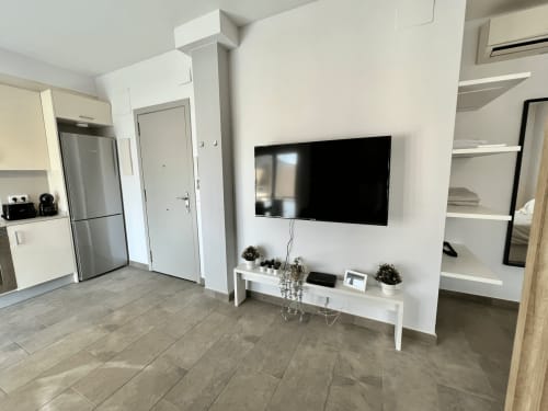 Sala de estar moderna en J&A APARTMENTS Terrassa con TV colgada, estanterías blancas, cocina y piso de baldosas