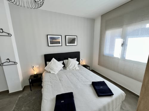 Dormitorio moderno en J&A Apartments en Terrassa con cama queen, cabecero negro, ropa de cama blanca y amplias ventanas