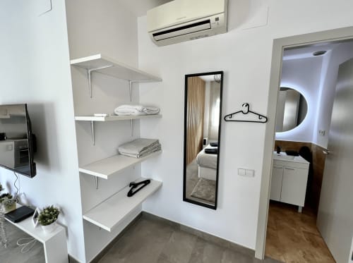 Armario moderno con estanterías blancas, espejo y perchas en los Apartamentos J&A en Terrassa
