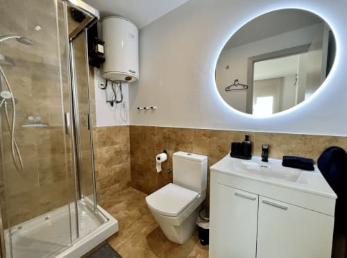 Baño moderno en J&A Apartments Terrassa con ducha, inodoro, espejo iluminado y vanidor blanco