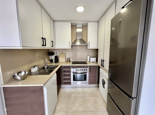 Cocina moderna en los Apartamentos J&A Terrassa con muebles blancos y marrón, electrodomésticos de acero inoxidable y encimeras beige
