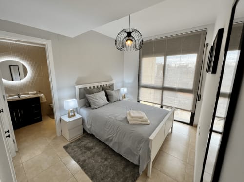 Dormitorio moderno en J&A Apartments en Terrassa con cama blanca, ropa de cama gris, lámpara colgante y puertas de cristal a la terraza