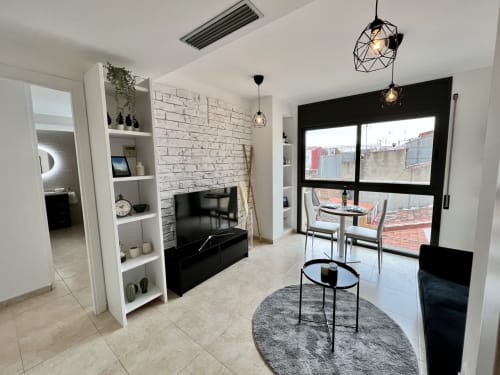 Moderna sala de estar de los Apartamentos J&A en Terrassa con estanterías blancas, chimenea, televisor y acceso a terraza