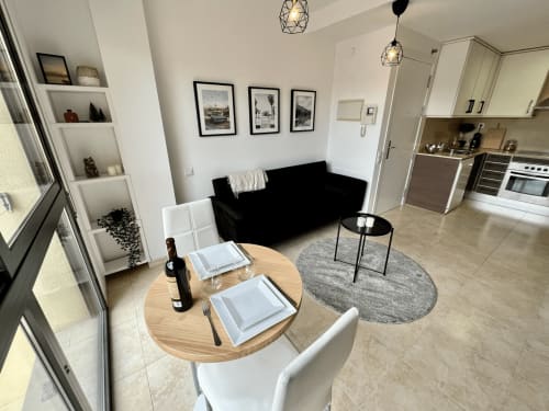Sala de estar moderna en J&A Apartments de Terrassa con sofá negro, mesa de comedor, cocina y estantería blanca