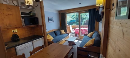 Appartement douillet à CMD Méribel Le Pralin avec intérieur en bois, coin salon bleu, table à manger, kitchenette et balcon