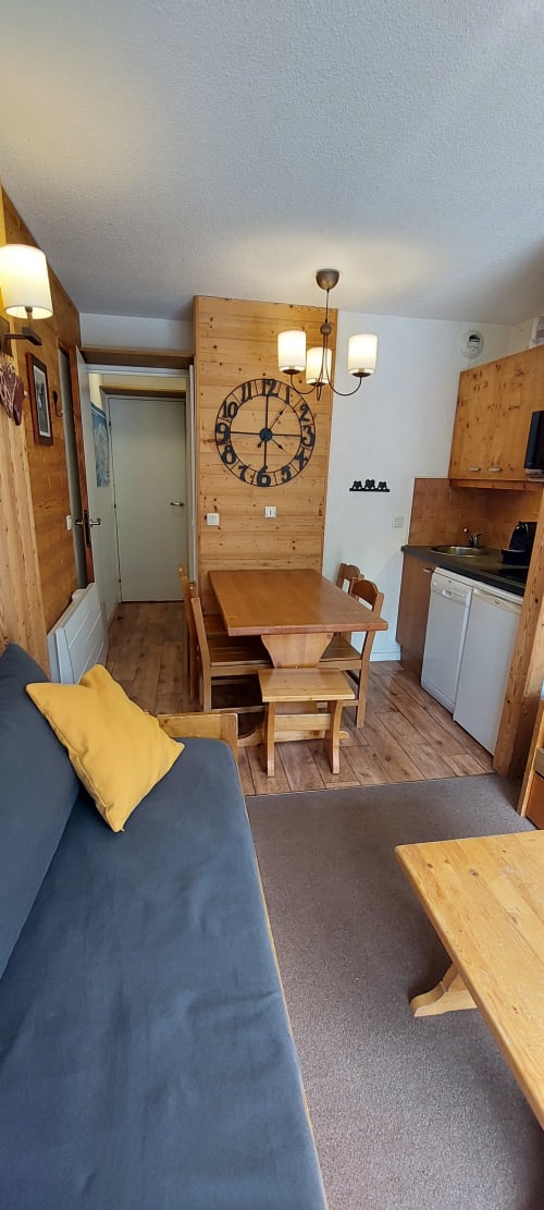 Séjour confortable à CMD Méribel Le Pralin avec mobilier en bois, table à manger, canapé bleu, cuisine et grandes