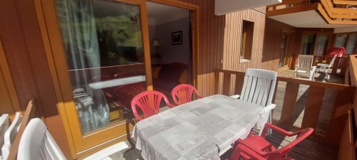 Salle à manger ensoleillée avec chaises rouges à table en bois, vue sur les montagnes par les portes vitrées, appartement CMD Méribel Le Pralin