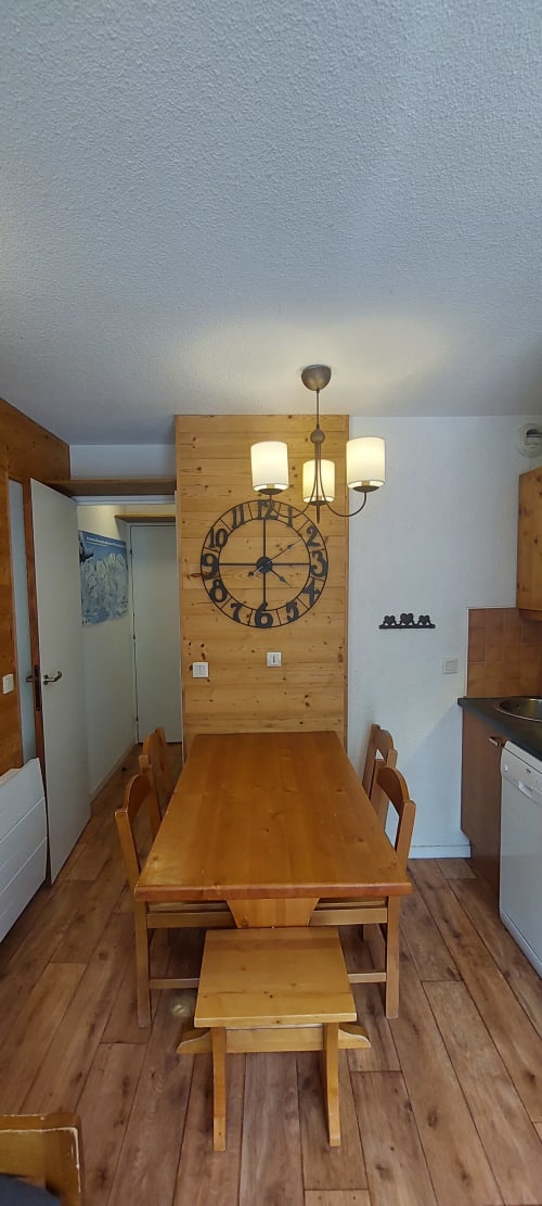 Table à manger en bois et chaises dans la cuisine de l'appartement CMD Méribel Le Pralin, avec horloge murale et luminaires suspendus