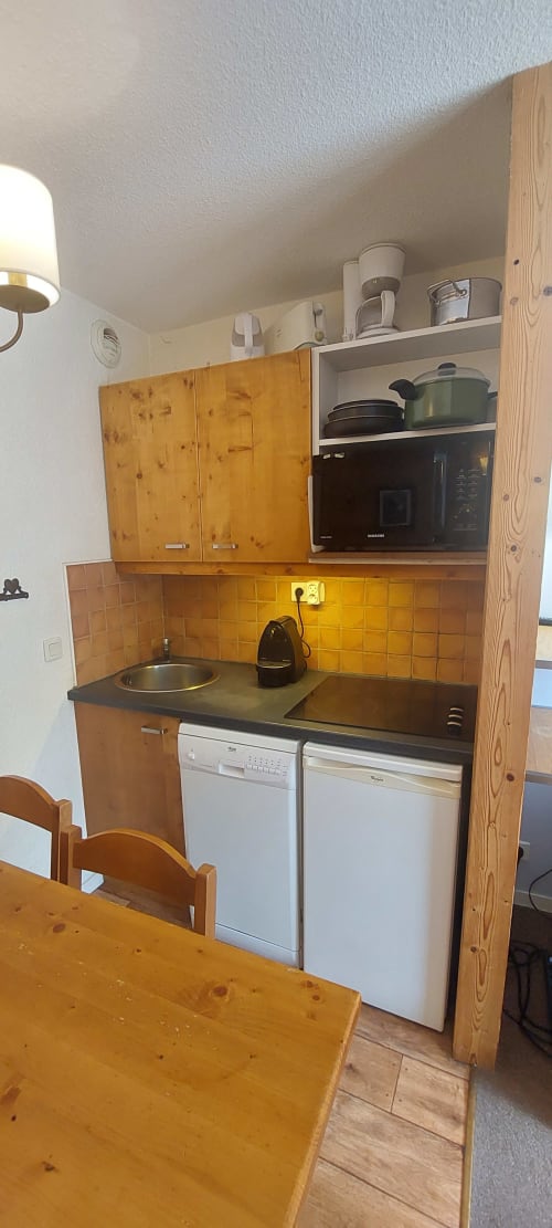 Petite kitchenette de l'appartement CMD Méribel Le Pralin avec meubles en bois, cuisinière, lave-vaisselle et four à micro-ondes