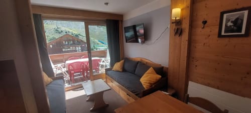 Séjour douillet à Méribel avec murs en bois, balcon vue montagne, salon confortable, TV et coin repas