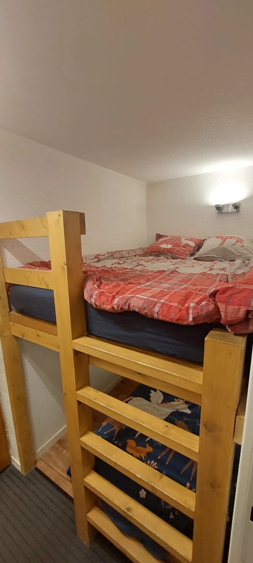 Lit superposé en bois avec literie rouge dans la chambre de l'appartement à Méribel, étagères de rangement en dessous, murs blancs, éclairage lumineux
