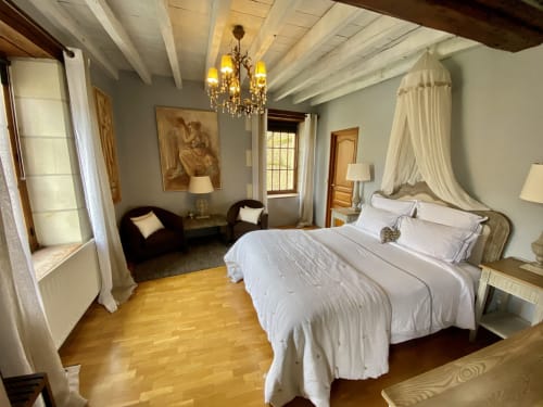 Chambre élégante au Moulin De La Chevrière avec lit à baldaquin, lustre en cristal et poutres apparentes