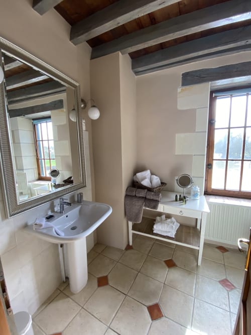 Salle de bains spacieuse au Moulin De La Chevrière B&B à Saché avec lavabo sur colonne, miroir, coiffeuse et poutres apparentes