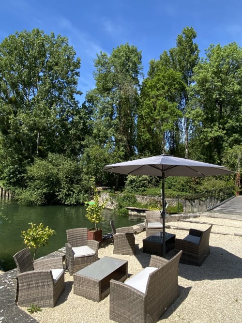 Terrasse extérieure avec mobilier en rotin et parasol avec vue sur la rivière au Moulin De La Chevrière, Saché