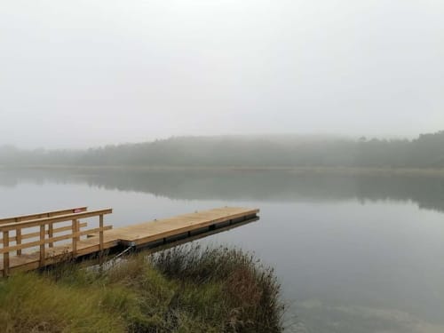 Cais de madeira estendendo-se em lago enevoado com margens gramadas perto de Óbidos, Portugal