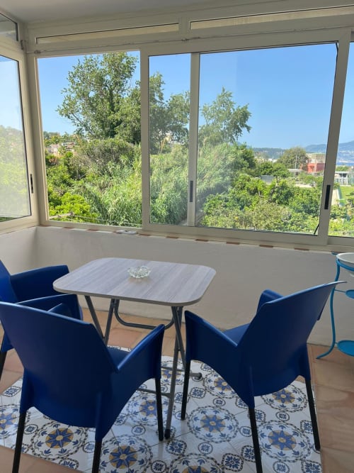 Luminosa lounge moderna a Palazzo Porta B&B Procida con sedie blu, vista sulla baia dalle ampie finestre che si affacciano su rigogliosi giardini