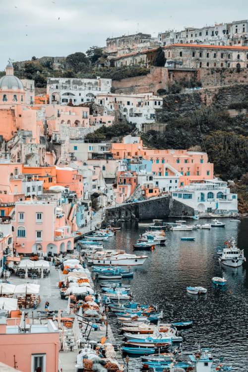 Vista colorata del porto di Procida con barche da pesca, edifici rosa e architettura costiera a Palazzo Porta