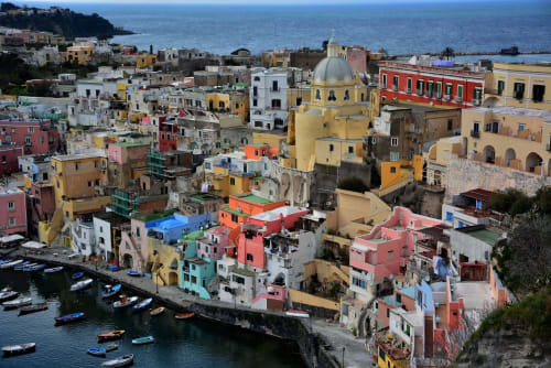 Coloratissimi edifici sul waterfront e chiesa con cupola a Procida, incantevole villaggio costiero italiano con barche e mare Mediterraneo