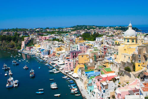 Isola colorata di Procida con edifici pastello, chiesa dalla cupola gialla e porto blu con barche