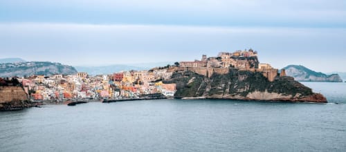 Gli edifici colorati del lungomare di Procida con le rovine del castello sulla collina che dominano il Mar Mediterraneo