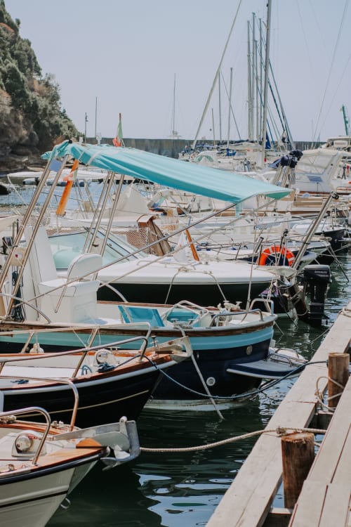 Barche a vela e pescherecci ormeggiati nel porto di Procida con tende turchesi e costa rocciosa