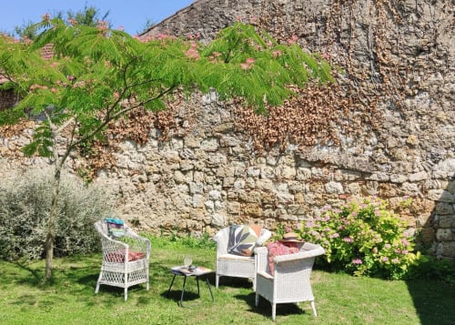 Salon de jardin du Rêve d’Alice installé sur la pelouse, au pied d’un mur en pierre ancien