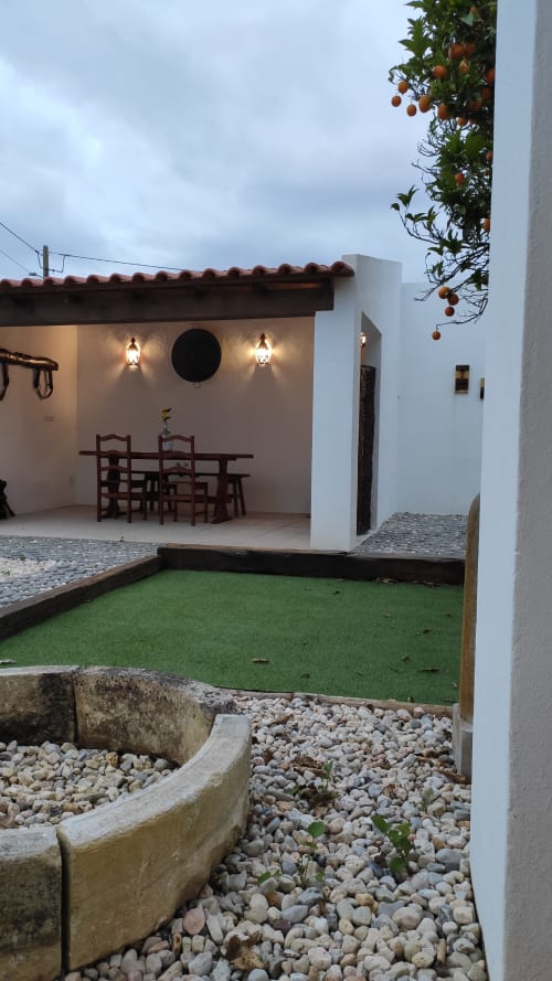 Cozy cottage patio in Óbidos with dining area, green lawn, orange tree, and white stone walls under cloudy sky