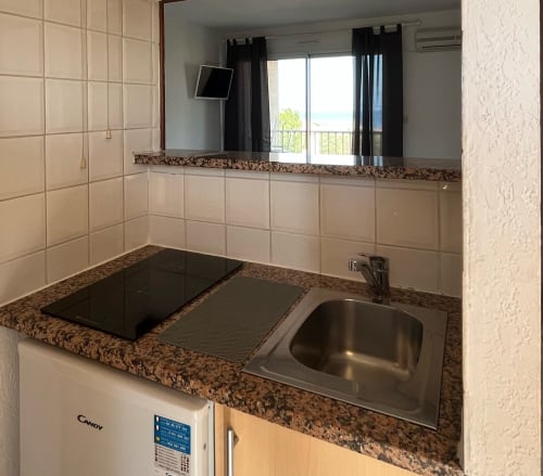 Petite cuisine moderne avec plan de travail en granit, plaque de cuisson électrique, évier et micro-ondes à la Résidence Saint Michel, L'île Rousse