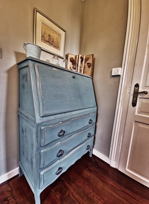 Secrétaire peinte en bleu avec tiroirs dans la chambre du Manoir Le Coutureau, décorée de livres et cadres