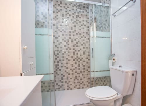 Baño moderno con mampara de ducha de cristal, azulejos mosaico, inodoro y lavamanos en apartamento de Puerto Santa María
