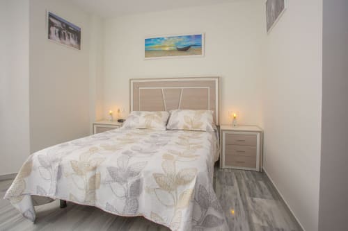 Dormitorio luminoso en apartamento de Puerto Santa María con cama matrimonial, ropa de cama beige, mesitas modernas y obra costera