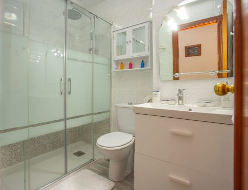 Baño moderno con ducha de cristal, lavabo blanco, inodoro y espejo en el apartamento Wehost Costaluz de Sanlúcar, España