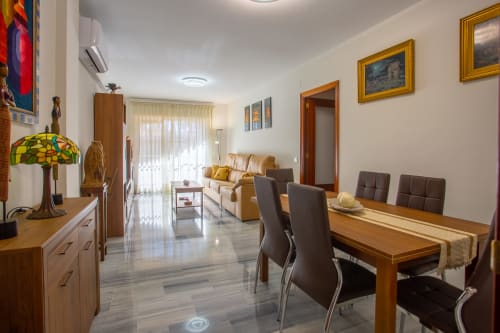 Apartamento moderno en Puerto Santa María con mesa de comedor de madera, sillas marrones, sofá beis y lámpara Tiffany en sala abierta