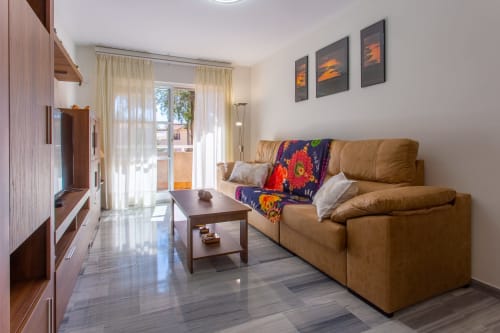 Moderna sala de estar con sofá de cuero color beige, manta colorida, mesa de centro, TV de pantalla plana y vistas al balcón en Puerto Santa
