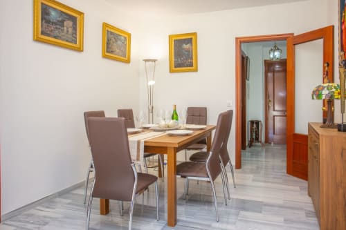 Comedor moderno en apartamento de Puerto Santa María con mesa de madera, sillas marrones, cuadros decorativos y acceso a sala de estar