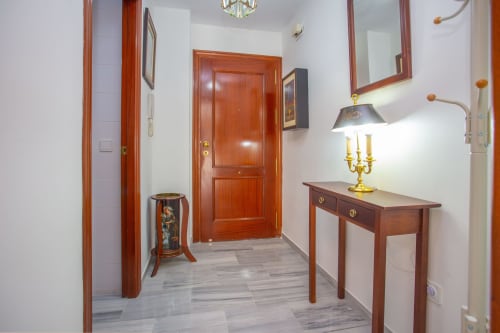 Entrada moderna de apartamento en Puerto Santa María con puertas de madera, consola, lámpara de latón y piso de baldosas