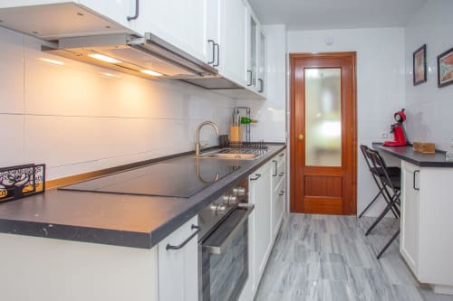 Moderna cocina de galera con encimeras negras, armarios blancos, electrodomésticos de acero inoxidable y área de comedor en Puerto Santa