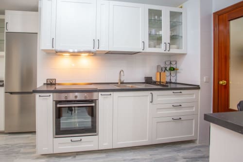 Cocina moderna blanca con encimeras oscuras, electrodomésticos de acero inoxidable y comedor en apartamento de Puerto Santa María