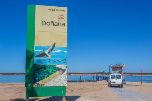 Letrero de entrada al Parque Nacional Doñana en la playa de Puerto Santa María con aguas azules e imágenes de fauna silvestre