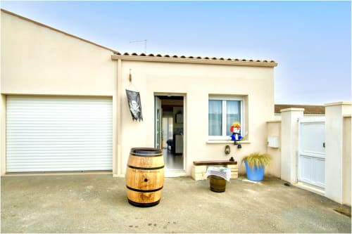 Entrée du gîte Le Pirate Benèze à Trizay avec garage, pot de fleurs bleu et décor rustique en tonneau