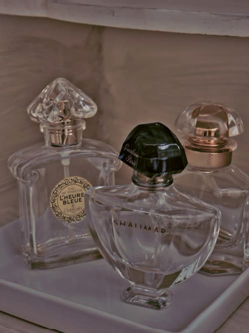 Trois élégants flacons de parfum exposés sur une surface blanche au Manoir Le Coutureau, présentant L'Heure Bleue et Shalimar