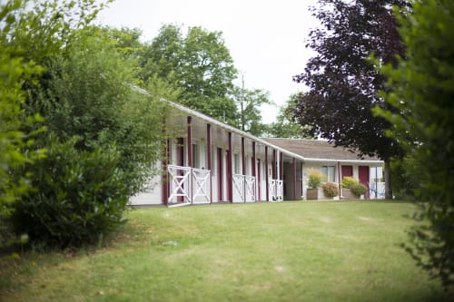 Façade de l'hôtel Mape à Dampierre en Burly avec portes rouges, encadrement blanc et pelouse soignée entourée d'arbres