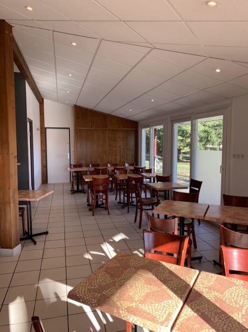 Salle à manger lumineuse de l'Hôtel Mape à Dampierre-en-Burly avec tables en bois, chaises orange et vue sur le jardin
