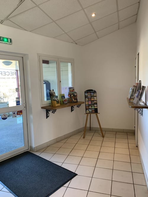 Entrée de l'hôtel Mape à Dampierre-en-Burly avec sol carrelé, étagères en bois et présentoir promotionnel