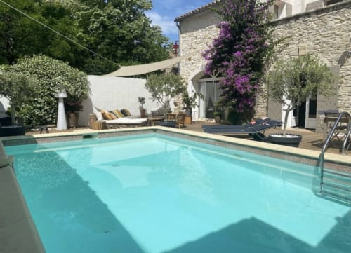 Türkisfarbenes Schwimmbad mit Steingebäude, violetten Bougainvilleen und Loungebereich in La Conciergerie De Franck in Boissieres